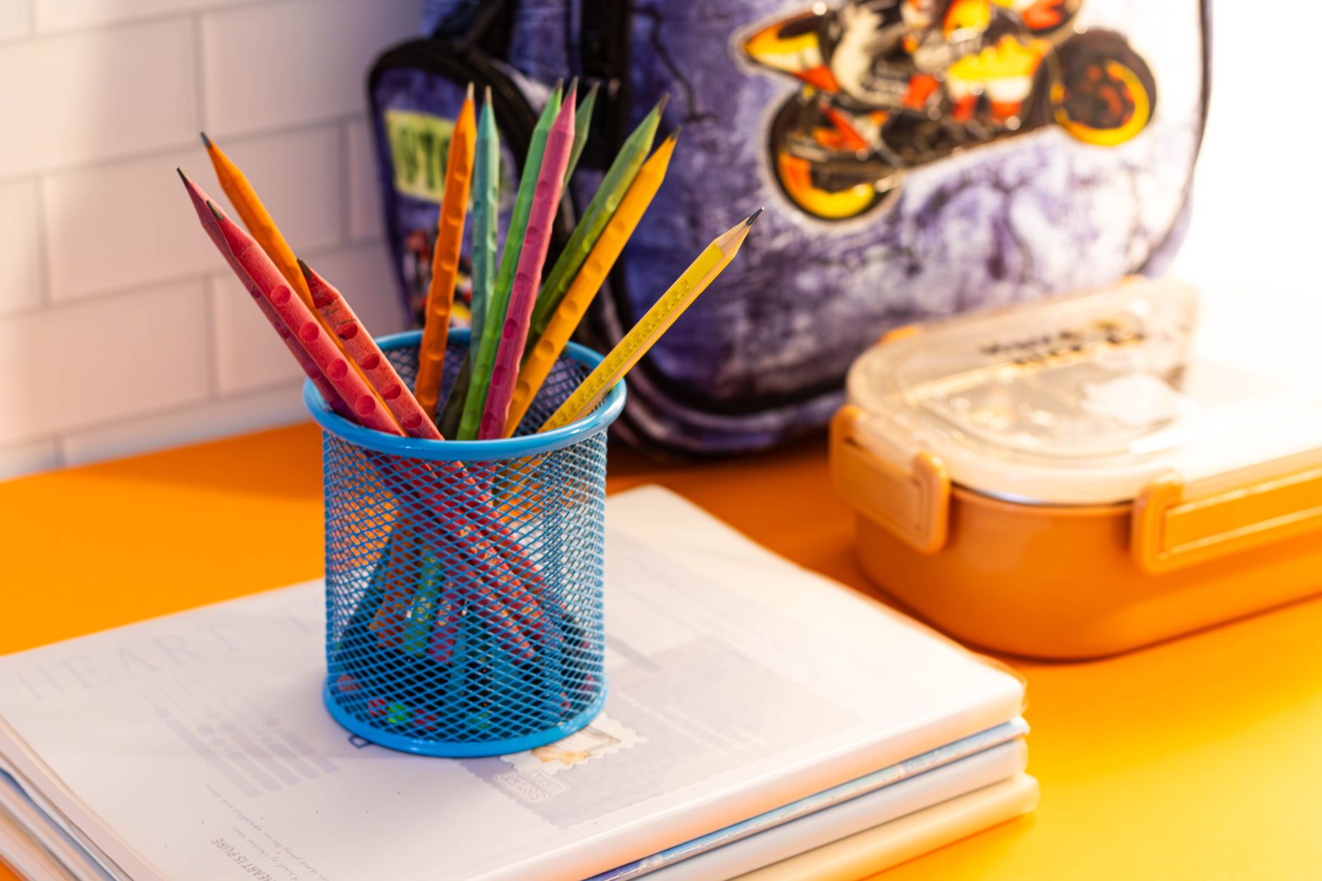 Fournitures scolaires animées comprenant des crayons, des cahiers et un sac à dos sur un bureau de salle de classe.