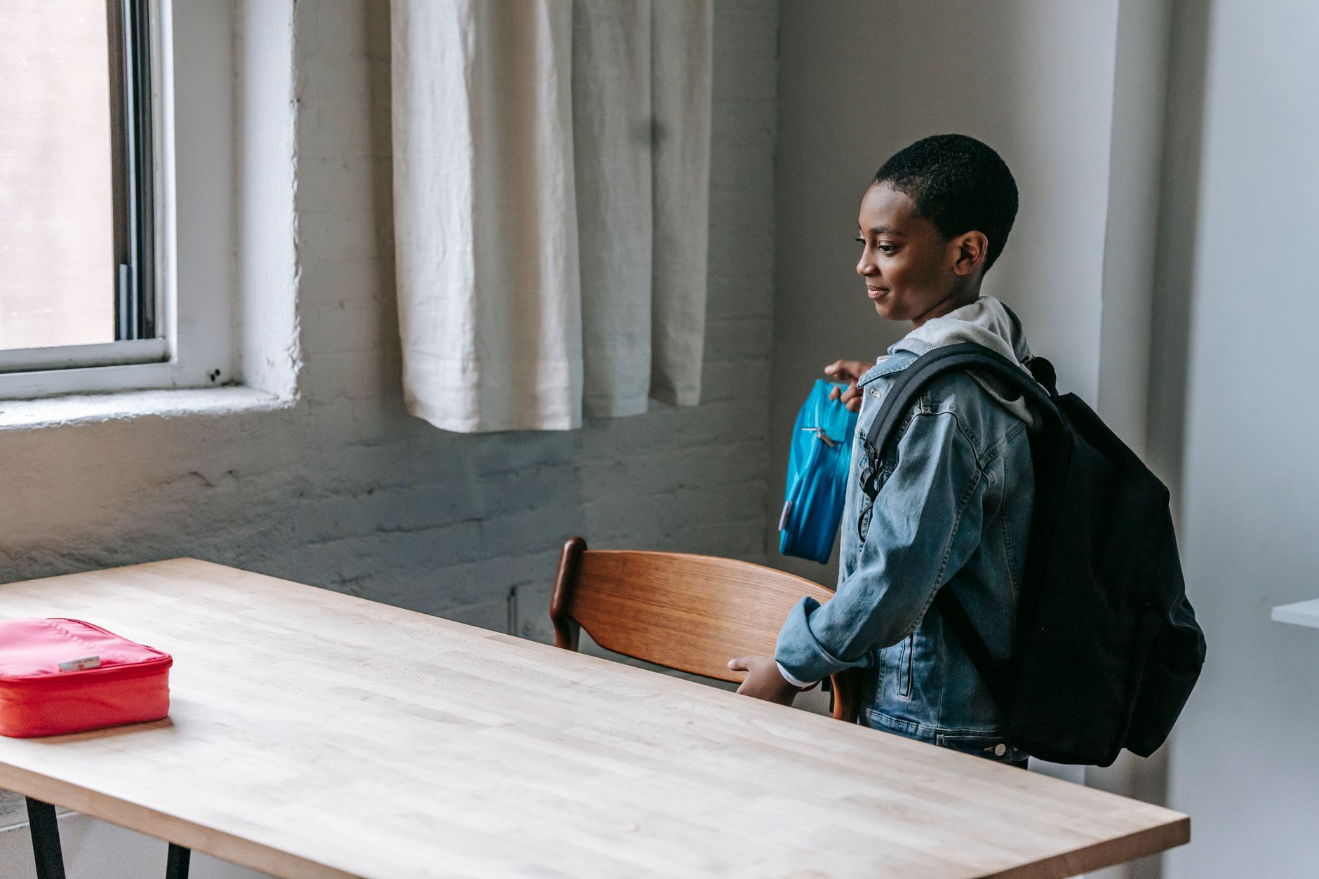 Vue de côté d'un enfant afro-américain mignon tenant une boîte à lunch tout en se préparant pour une collation à l'école