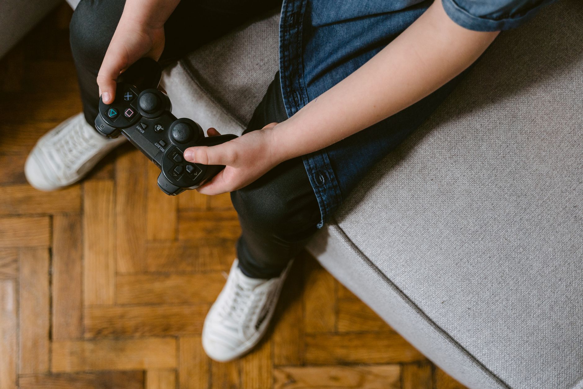 Mains d’enfant tenant une manette de jeu sur un canapé