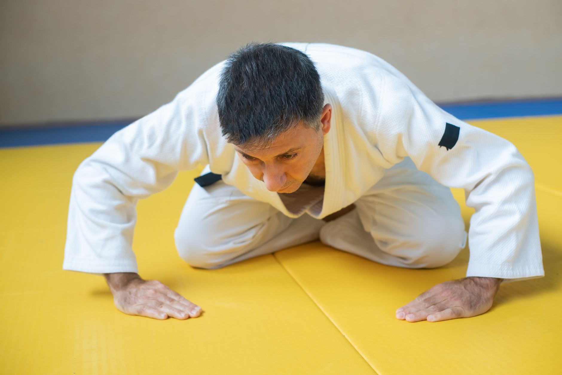 Judoka en kimono blanc, à genoux sur un tatami jaune, effectuant le salut traditionnel
